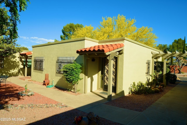 exterior space featuring a tiled roof, a pergola, and stucco siding