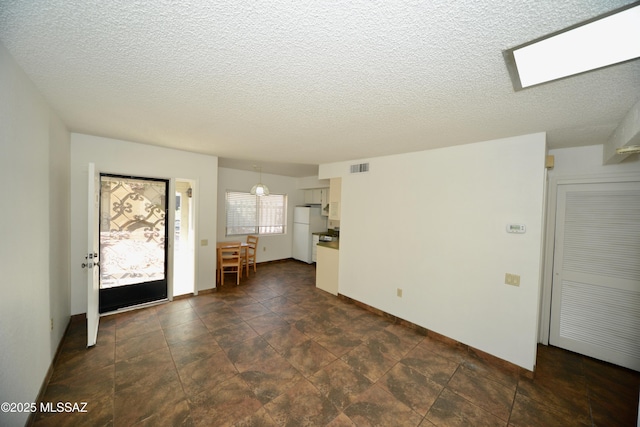 interior space featuring baseboards, a textured ceiling, and visible vents