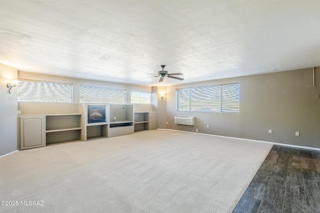 unfurnished living room with carpet floors, an AC wall unit, ceiling fan, and baseboards