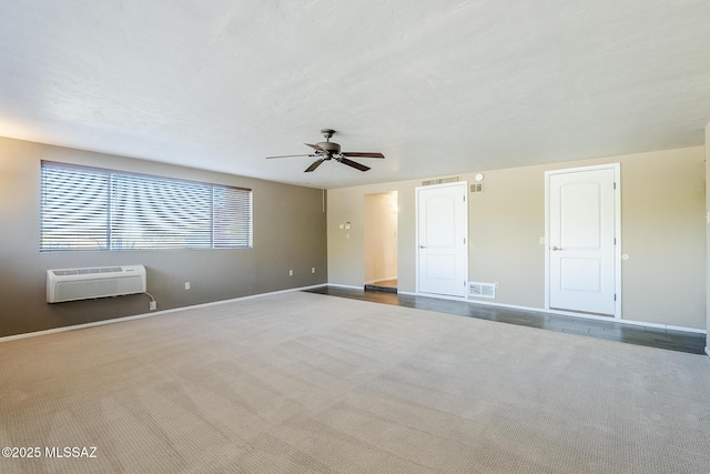 carpeted spare room featuring an AC wall unit, baseboards, ceiling fan, and visible vents