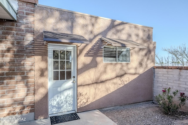 property entrance with fence, stucco siding, and brick siding