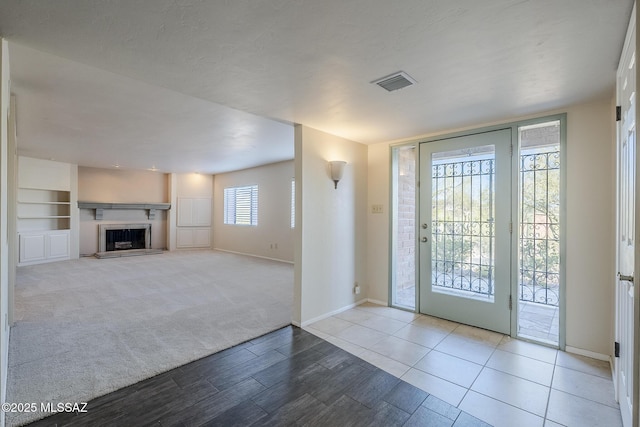 foyer with a fireplace with raised hearth, baseboards, visible vents, and wood finished floors