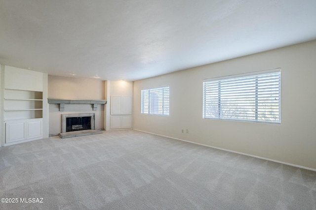 unfurnished living room with baseboards, a fireplace with raised hearth, and light carpet