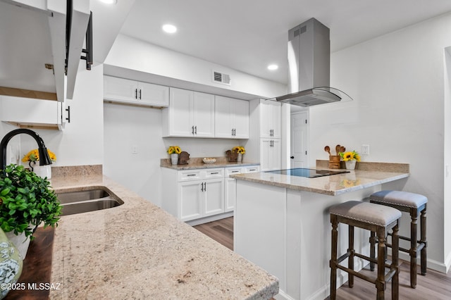 kitchen featuring black electric stovetop, a peninsula, island range hood, wood finished floors, and visible vents