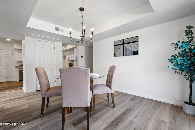 dining space with a tray ceiling, visible vents, baseboards, and light wood-style floors