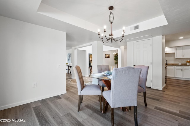 dining area with dark wood-style flooring, a chandelier, visible vents, and a raised ceiling