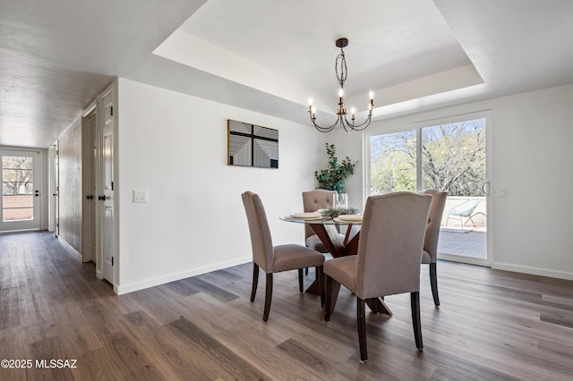 dining area with an inviting chandelier, a tray ceiling, dark wood-type flooring, and a healthy amount of sunlight