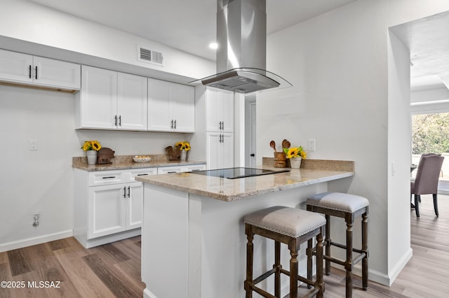 kitchen featuring white cabinets, light stone countertops, baseboards, island exhaust hood, and wood finished floors