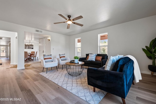 living area with visible vents, baseboards, ceiling fan with notable chandelier, and light wood-type flooring