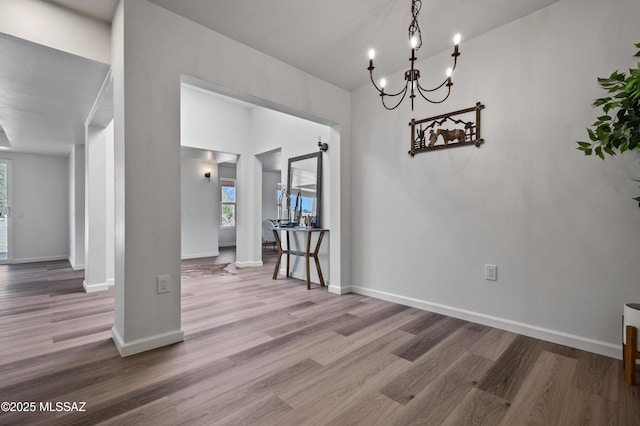 unfurnished dining area featuring an inviting chandelier, baseboards, and wood finished floors