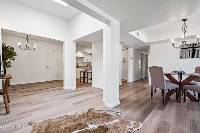dining space with an inviting chandelier, baseboards, and light wood-type flooring