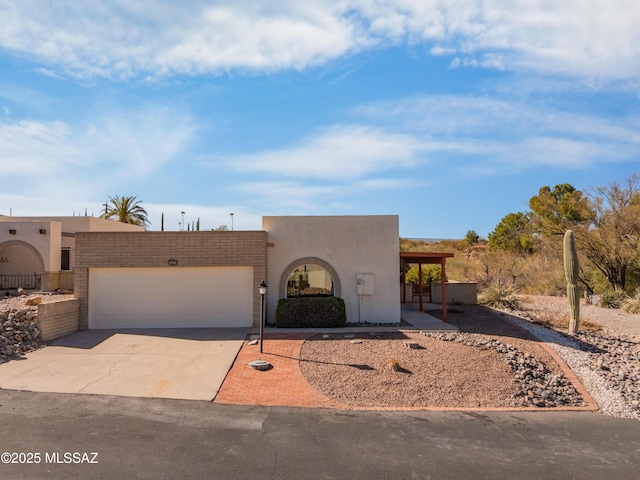 pueblo-style home with an attached garage, driveway, and stucco siding