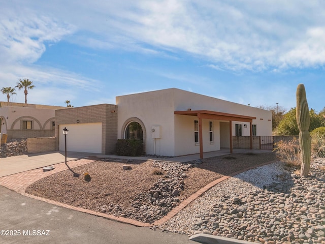pueblo revival-style home featuring fence, an attached garage, stucco siding, and concrete driveway