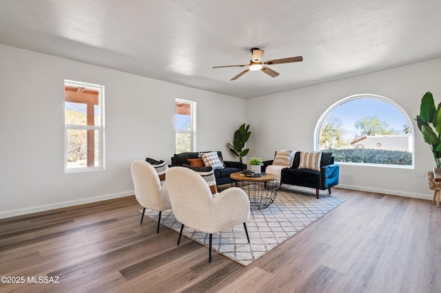 living area with baseboards, ceiling fan, and wood finished floors