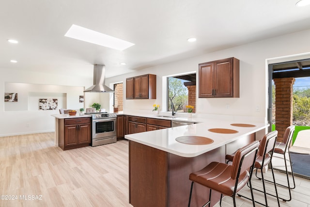 kitchen with wall chimney range hood, a peninsula, appliances with stainless steel finishes, and plenty of natural light