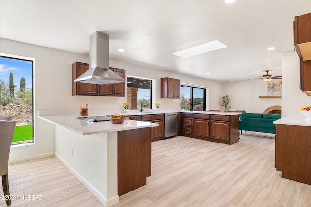 kitchen with light countertops, a peninsula, a sink, and island exhaust hood