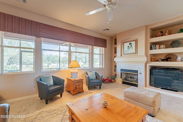 living area featuring visible vents, a healthy amount of sunlight, baseboards, a tiled fireplace, and a ceiling fan