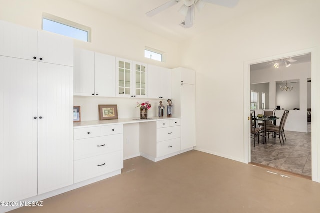 bedroom featuring a towering ceiling, built in desk, baseboards, ceiling fan with notable chandelier, and concrete floors