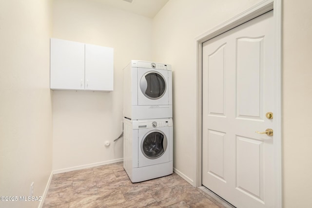 clothes washing area featuring baseboards, stacked washer and dryer, and cabinet space