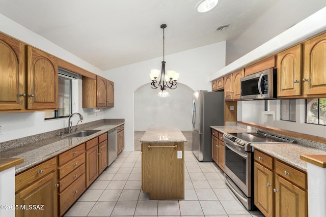 kitchen with a center island, a sink, arched walkways, decorative light fixtures, and appliances with stainless steel finishes