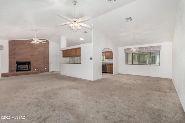 unfurnished living room with ceiling fan with notable chandelier, a brick fireplace, visible vents, light colored carpet, and vaulted ceiling