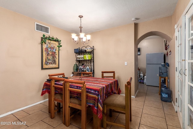 dining area with light tile patterned floors, a notable chandelier, visible vents, baseboards, and arched walkways