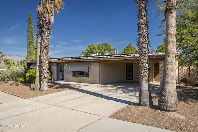 view of front of property featuring fence, brick siding, concrete driveway, a carport, and metal roof