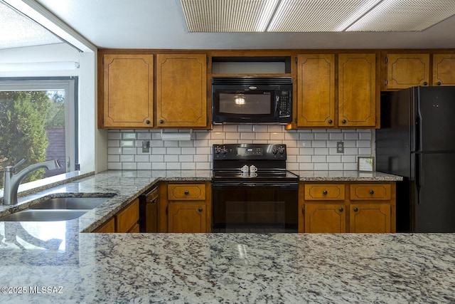 kitchen with light stone countertops, a sink, brown cabinetry, backsplash, and black appliances