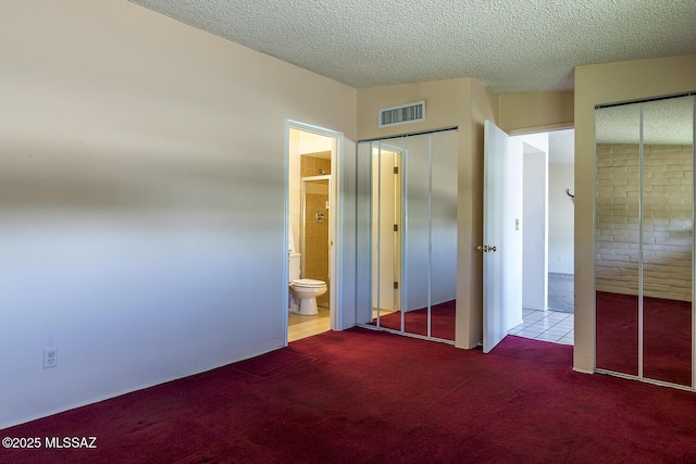 unfurnished bedroom featuring a textured ceiling, visible vents, carpet, and ensuite bath
