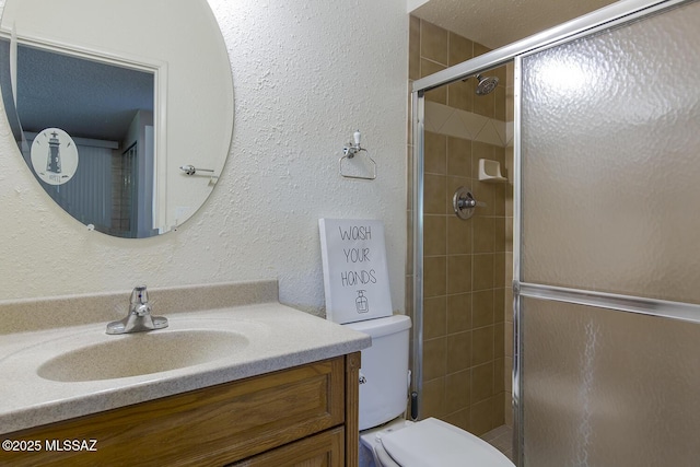 bathroom featuring vanity, a textured wall, a shower stall, and toilet