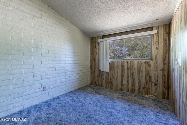 carpeted empty room with a textured ceiling, wood walls, and vaulted ceiling