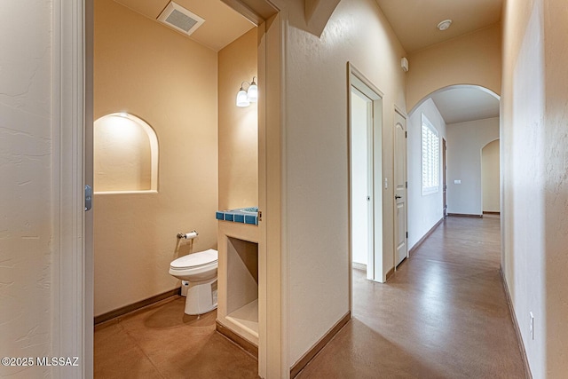 hallway featuring arched walkways, baseboards, and visible vents