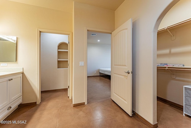 interior space with vanity, baseboards, a walk in closet, and visible vents