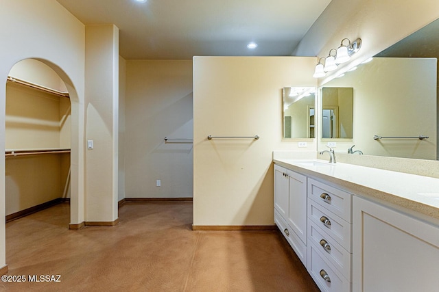 bathroom with a sink, a walk in closet, baseboards, and double vanity