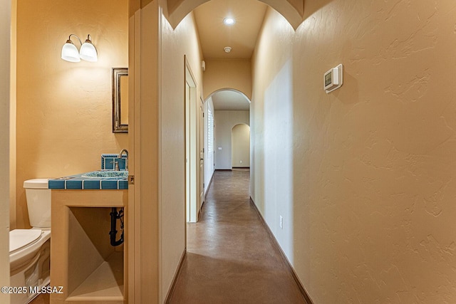 hall with arched walkways, a textured wall, baseboards, and concrete flooring