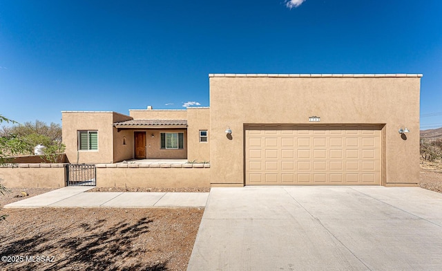 pueblo-style home with fence, stucco siding, a gate, an attached garage, and driveway