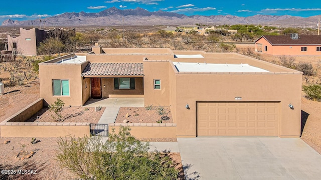 pueblo-style home with a garage, fence, stucco siding, concrete driveway, and a mountain view