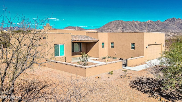 rear view of property featuring a garage, a mountain view, stucco siding, and a tiled roof