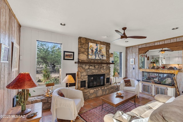 tiled living area with wooden walls, a fireplace, and a ceiling fan