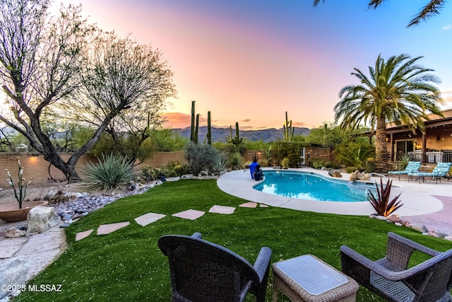 pool at dusk featuring a fenced in pool, a patio, a yard, and a fenced backyard
