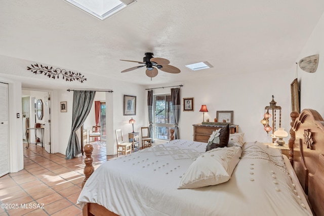bedroom with ceiling fan, light tile patterned floors, a skylight, and access to exterior
