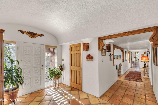 foyer entrance with light tile patterned floors, a textured ceiling, and lofted ceiling