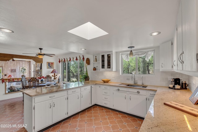 kitchen with a sink, a peninsula, white cabinetry, tasteful backsplash, and a skylight