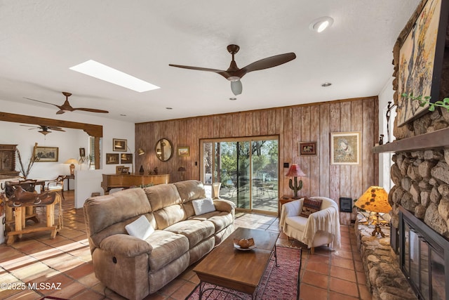 living area featuring tile patterned floors, a ceiling fan, and wood walls