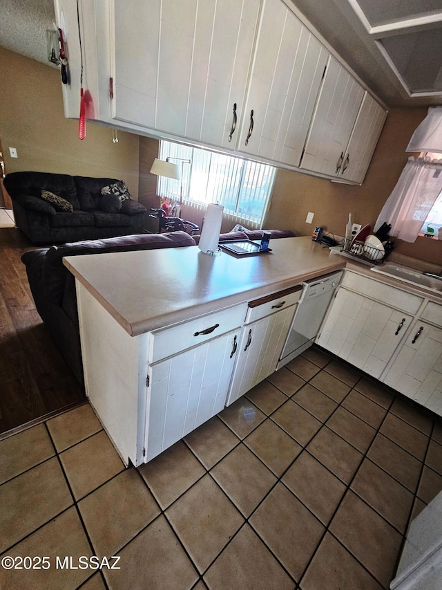 kitchen with white dishwasher, tile patterned floors, white cabinets, and light countertops