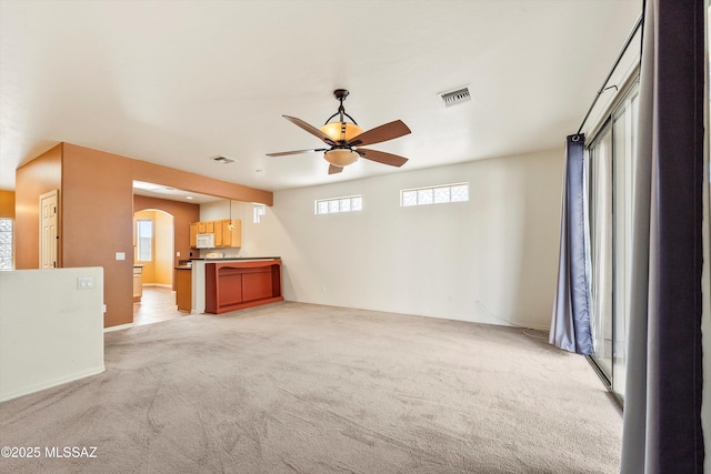 unfurnished living room featuring light colored carpet, visible vents, a ceiling fan, and arched walkways