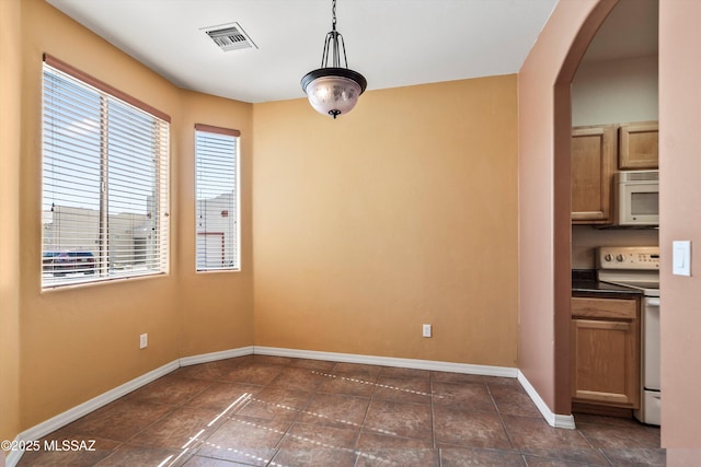 unfurnished dining area featuring dark tile patterned flooring, arched walkways, baseboards, and visible vents