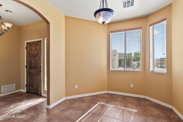 tiled empty room featuring arched walkways, baseboards, and visible vents