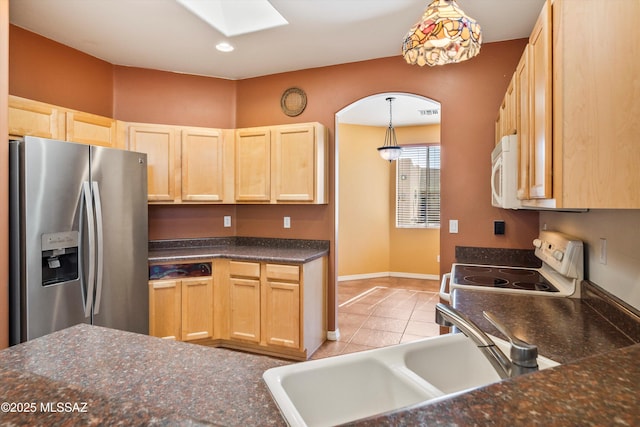 kitchen with light brown cabinets, white appliances, light tile patterned flooring, a sink, and a skylight