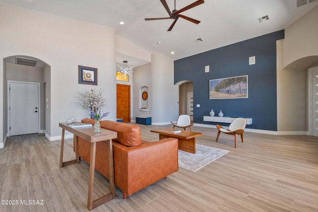 living area with high vaulted ceiling, visible vents, baseboards, ceiling fan, and arched walkways
